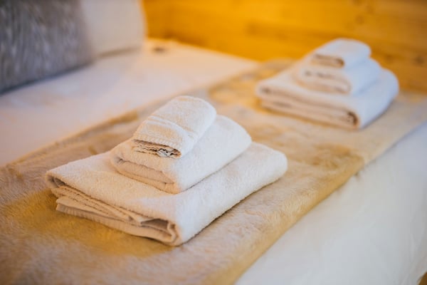 Neatly folded white towels stacked on a bed in a warm, clean room